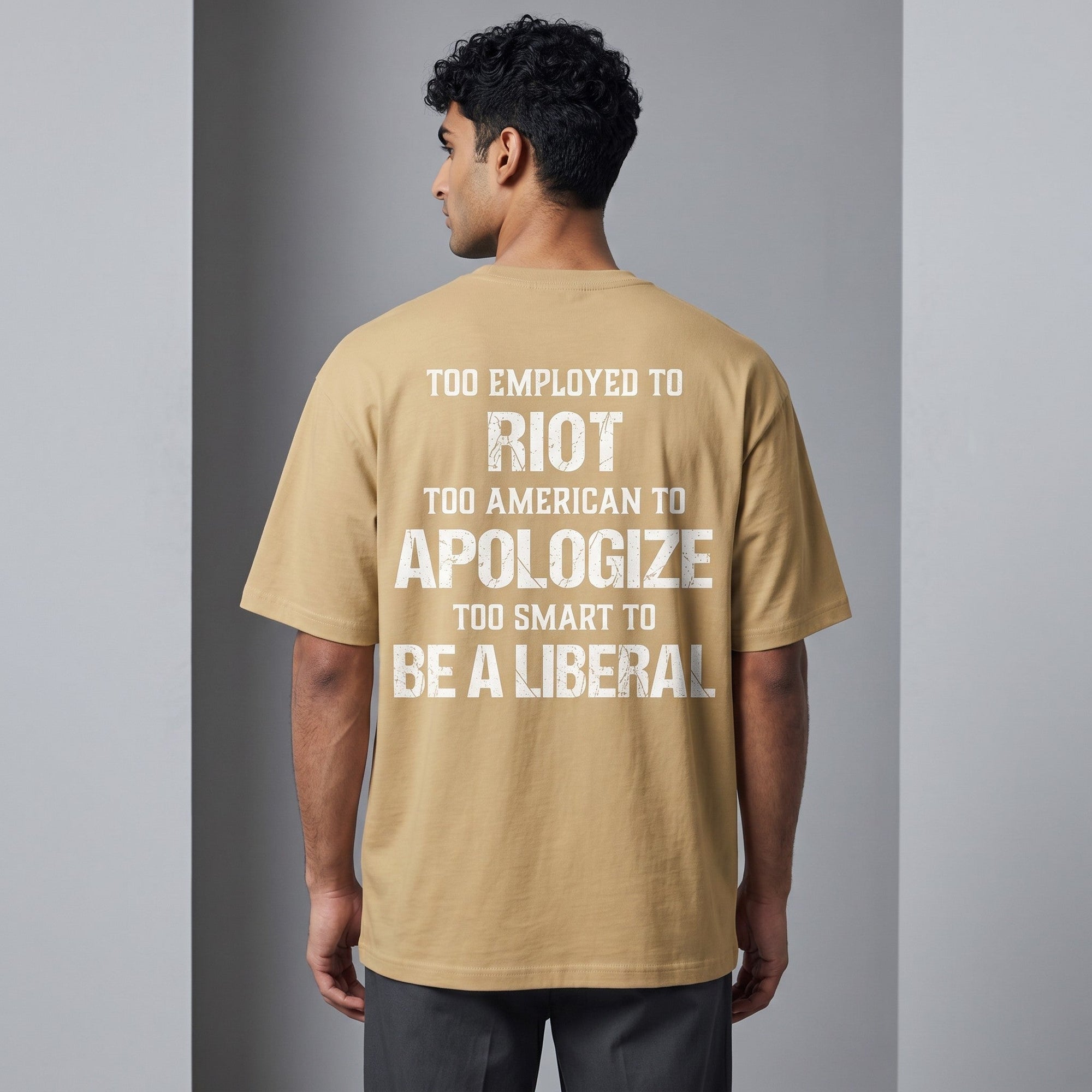 TrendyShift.Com tan oversized t-shirt with white distressed text print on the back, worn by a man from behind.